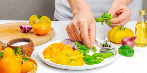 A woman is preparing a tomato salad. Ripe vegetables, herbs, aromatic spices, olive oil