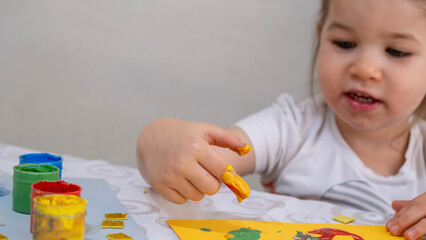 Happy smiling little girl enjoying creative finger painting activity, learning colors and shapes, improving fine motor skills through fun art and early childhood education.