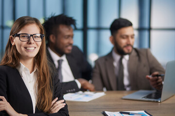 Attractive young woman smiling at camera while sitting together with another people at the table