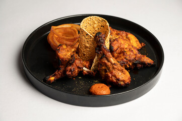 Tandoori Chicken marinated in yoghurt and home-ground spices, roasted over charcoal in a traditional clay oven — served on a plate with papad and onion salad on a white background.