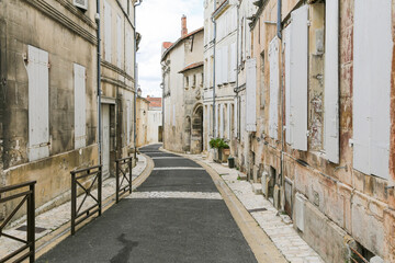 A narrow street with a blue sign on the left side in Cognac France