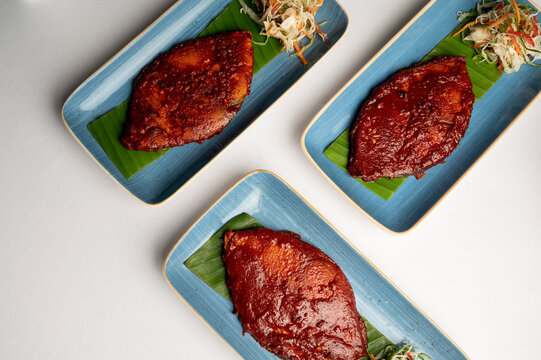 Three plates of Kingfish Recheado &mdash; Goan-style spicy stuffed kingfish served on banana leaves with salad, presented on blue plates against a white background.