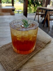 a glass of iced tea with rosemary leaf garnish on a wooden table