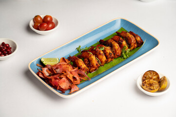 Prawns chili fry served on a banana leaf in a blue plate with salad, made with toddy vinegar, semolina coating, and tossed with onion, tomato, and green chilies.