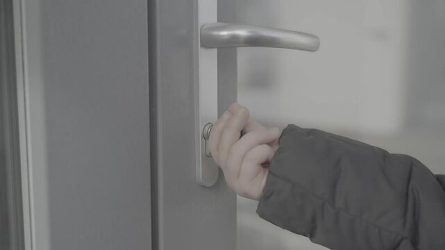 A child in a black jacket opens the handle of a glass door with key. Slog-3