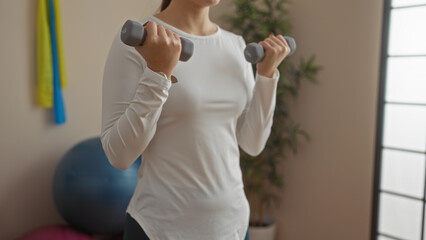 Woman exercising with dumbbells indoors at a gym, focused on strength training in a sports center...