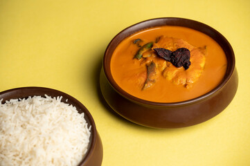 Fish Curry Rice — Kingfish cooked in traditional Goan curry infused with coconut milk and local spices, served with rice in brown pots on a yellow background.