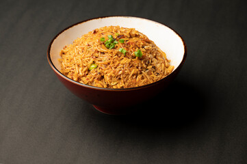 Vegetable fried rice prepared in Pan Asian style, served in a bowl on a black background, showcasing colorful vegetables and aromatic seasoning.