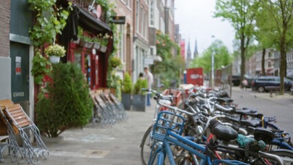 Blurred bicycles line a charming amsterdam street with vibrant shops and greenery, capturing the essence of urban life in the netherlands.