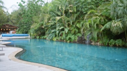 Blurry view of tropical resort pool and lush greenery with defocused pavilion in background exudes luxury and relaxation in outdoor hotel setting.