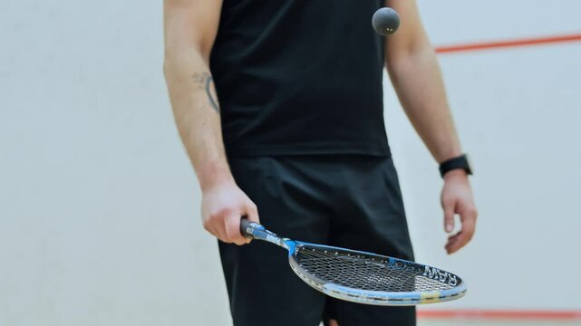 Focused male athlete balancing squash ball on racket before competitive match
