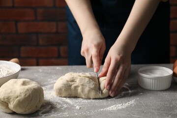 Woman cutting raw dough at light grey table, closeup