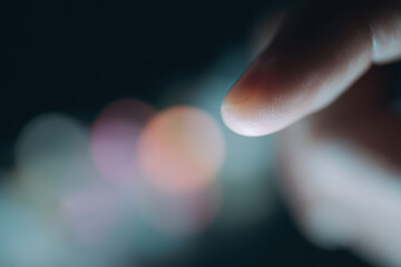 Close up of finger touching glowing screen with bokeh lights