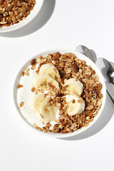 Serving Breakfast. Bowls of Greek Yogurt with Homemade Granola and Banana Slices on White Table. 