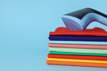 Upright steamer and stack of folded clothes on light blue background, closeup. Space for text