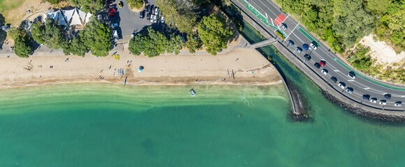 Aerial view of Mission Bay beach in Auckland, New Zealand. People are swimming, kayaking, and relaxing on the beach. Cars drive along the scenic Tamaki Drive. , AUCKLAND, NZ