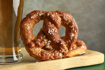 Tasty pretzels and glass of beer on green wooden table against grey background, closeup