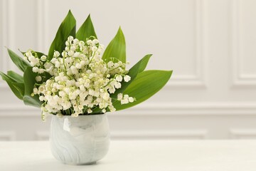 Beautiful lilies of the valley flowers in vase on white table. Space for text