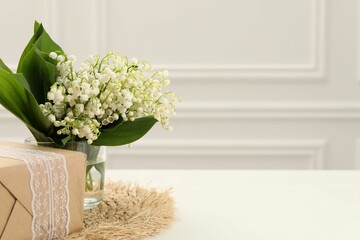 Beautiful lilies of the valley flowers and gift on white table. Space for text
