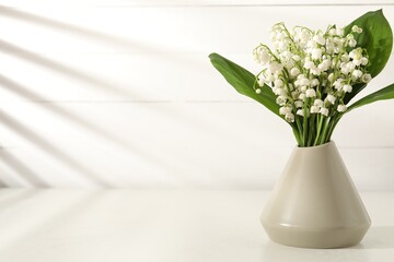 Beautiful lilies of the valley flowers in vase on white table. Space for text