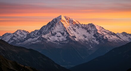 Snow capped mountain peak at sunset with orange and pink sky.