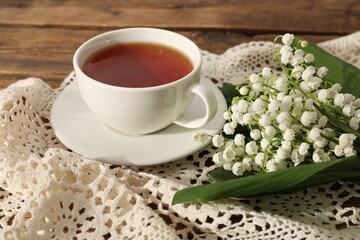 Beautiful lilies of the valley flowers and tea on wooden table, closeup