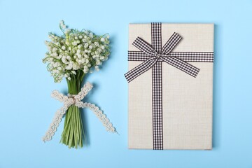 Beautiful lily-of-the-valley flowers and gift on light blue background, top view