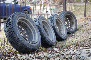 Four car wheels with winter tires, a chain link fence. Replacing winter tires with summer tires in...