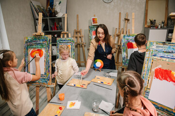 Teacher learn children to draw pictures in an art lesson. Artist explains how to mix and combine colors. Childs painting in workshop. Kids drawing brush on easel. Education, learning concept.