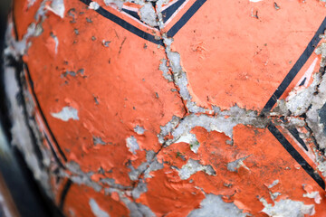A close-up shows a fragment of an old, worn-out soccer ball. The orange surface is cracked and peeling, revealing a white base along the black lines.
