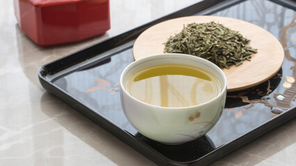 a glass of green tea in the foreground. tea leaf green loose on a plate in the background