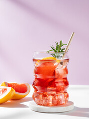 Refreshing mocktail with grapefruit, rosemary and ice in a glass on a white pink background.