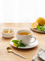 Cup of herbal tea with lemon, honey and mint on wooden tabletop with citrus fruits
