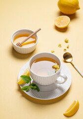Cup of herbal tea with lemon, honey and mint on yellow background with citrus fruits and morning shadows.