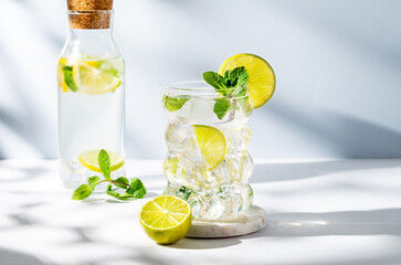 Mojito cocktail in a glass with lime, mint and ice on a white blue background with shadow and bottle.