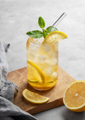 Iced tea with lemon and mint in a glass on a wooden board on a light background