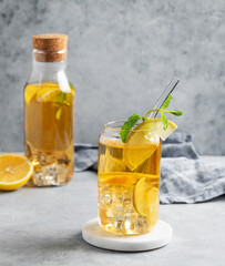 Iced drink with lemon and mint in a glass and bottle on a light background with shadows