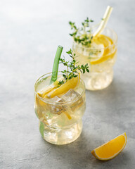 Two glasses of lemonade with fresh lemon, thyme and ice on a light background with sunlight.