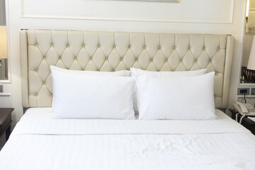 A warmly cozy toned cream bedroom featuring a white bed, pillows, and blanket in a hotel room