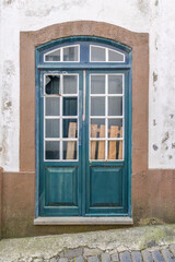 Weathered Teal Door with Broken Glass and Wooden Planks. Close-up of an aged teal double door with broken glass panes partially covered by wooden planks, set within a weathered stone and plaster frame