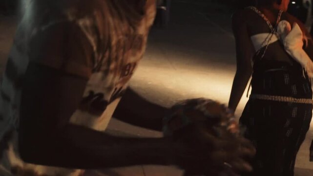 Orchestra dancer hitting a traditional tambourine during a night ceremony in Casamance, Senegal &mdash; rhythmic moment under event lighting, cultural celebration with music, movement and percussion