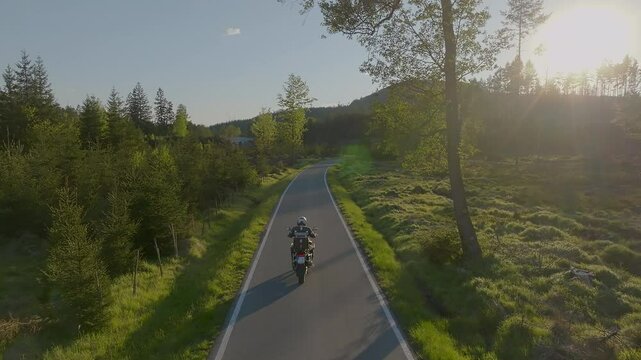 Driver riding motorcycle on empty asphalt road, spring mountains during sunset