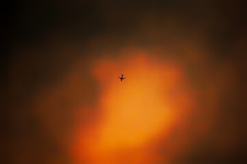 Dramatic cloudscape with bright orange and yellow hues, featuring a tiny airplane silhouetted against the sunset.