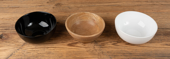 Three empty bowls on table, white porcelain, black and wooden dishes on tabletop, rustic dish