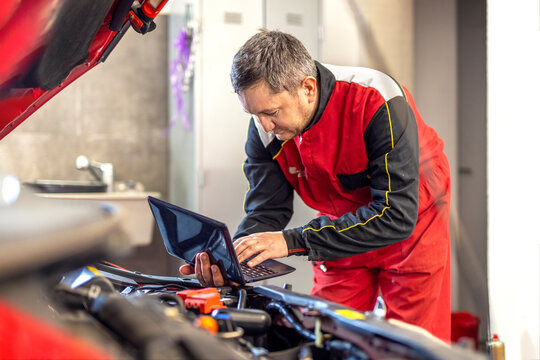 Car mechanic performing engine adjustment and repair using laptop. Man working with modern technology during car maintenance. Service and inspection of vehicle