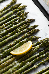Close up of grilled green asparagus with lemon on baking tray and hard cheese