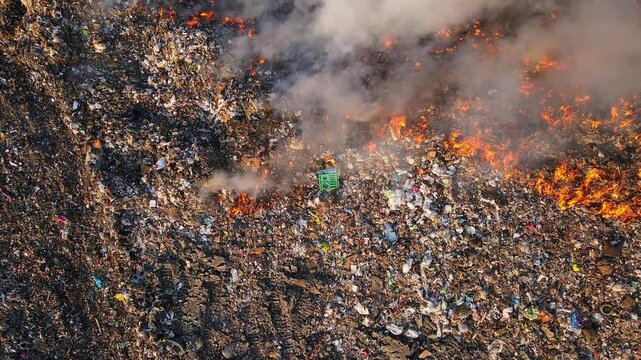 Raging fire spreads through landfill with dense smoke and visible waste piles