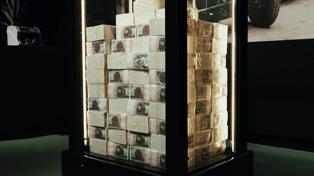 A wider view of a room with a glass box full of money, stored in a secure dark space, likely a bank vault or safe.