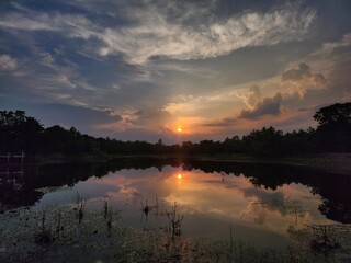 Serene sunset over a calm lake with vivid reflections, dramatic clouds, and silhouetted trees—perfect peaceful nature scene.