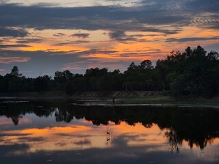 Serene sunset over a calm lake with vivid reflections, dramatic clouds, and silhouetted trees—perfect peaceful nature scene.